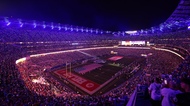 Les drapeaux des États-Unis et du Canada sur le terrain d'un stade de football plein à craquer.