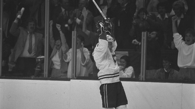 Photo noir et blanc d'un joueur de hockey sur une patinoire, qui l&egrave;ve les bras apr&egrave;s avoir marqu&eacute; un but.