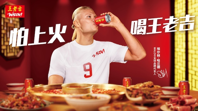Un joueur de soccer assis à une table couverte de nourriture boit une canette de thé.