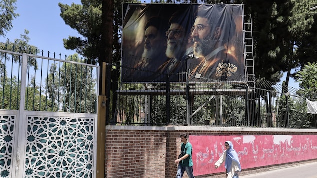 Des Iraniens passent devant un panneau d'affichage représentant le défunt guide suprême iranien, l'ayatollah Rouhollah Khomeiny, son successeur, le défunt ayatollah Ali Khamenei, et le nouveau guide suprême, Mojtaba Khamenei, devant l'ancienne ambassade des États-Unis à Téhéran, le 15 juin 2026.