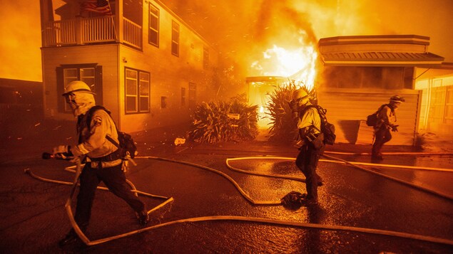 Firefighters run past a burning building.