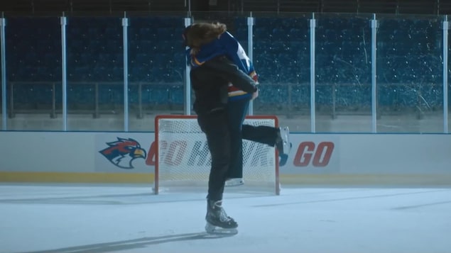 Une femme saute dans les bras d'un joueur de hockey sur une patinoire.