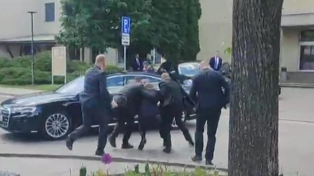 Des hommes traînent un autre homme, blessé, vers une voiture.