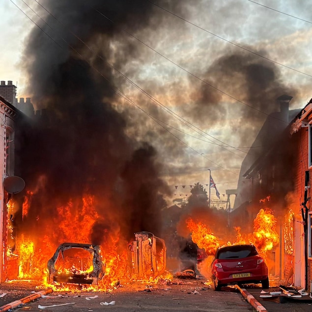 Des véhicules et des maisons en feu dans une rue de Belfast.