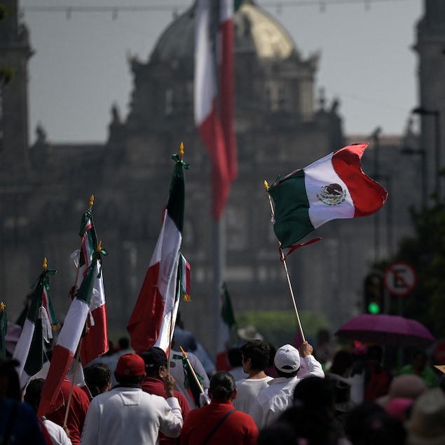 Des gens de dos marchent dans la rue en tenant des drapeaux mexicains.