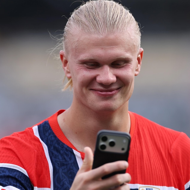 Erling Haaland regarde un cellulaire en souriant.