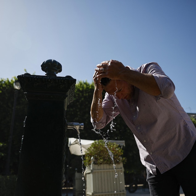 Un homme se rafraîchit en envoyant l'eau d'une fontaine sur sa tête.
