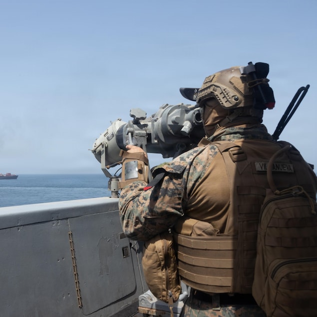 Un militaire observe un navire au loin avec un instrument d'optique.