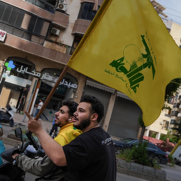 Dans une rue de Beyrouth, deux hommes sur un scooter brandissent un drapeau du Hezbollah.