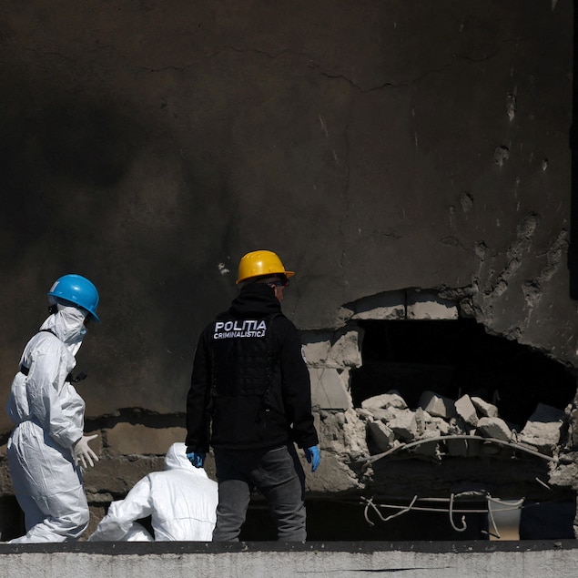 Des policiers et des experts roumains examinent un trou dans un mur causé par l'explosion d'un drone.