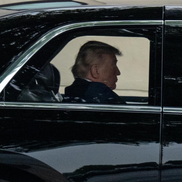 Donald Trump photographié de loin assis à l'arrière de la limousine présidentielle.
