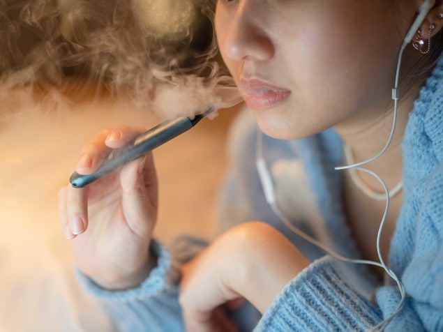 Une jeune femme fume une cigarette électronique.