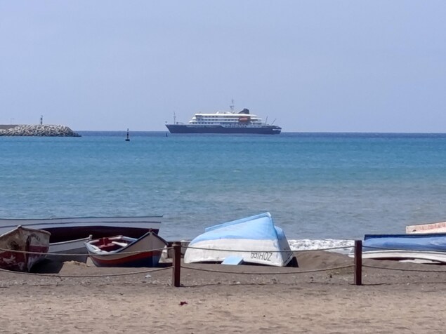 Un navire de croisière au large d'une plage où se trouvent des chaloupes.