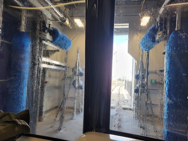 Une station de lavage du REM, avec des rouleaux bleus et des jets d'eau, vue de l'intérieur d'un wagon.