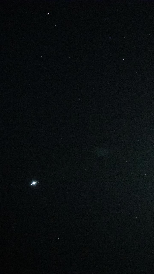 Photo sombre où on voit le relief de la lune et un petit point blanc, la planète Vénus.