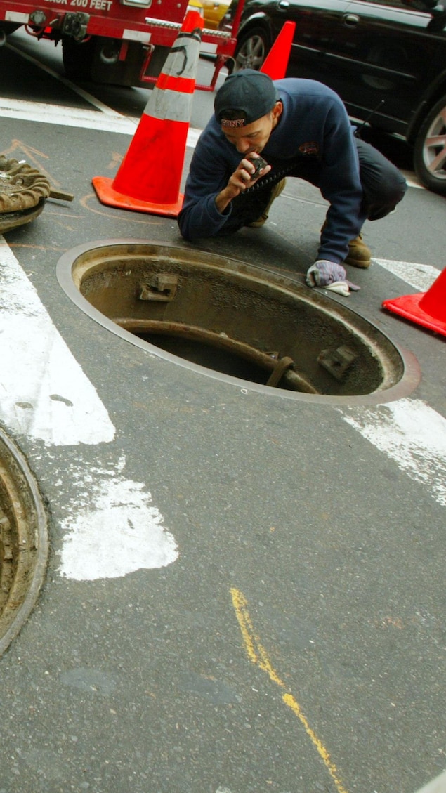 Un homme inspecte une bouche d'égout à New York.