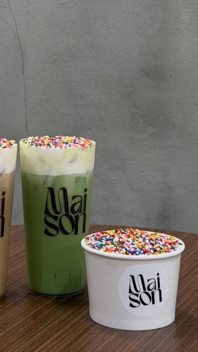 Un gâteau recouvert de bonbons colorés dans un gobelet de carton, à côté d'un verre de matcha lui aussi recouvert des mêmes bonbons.