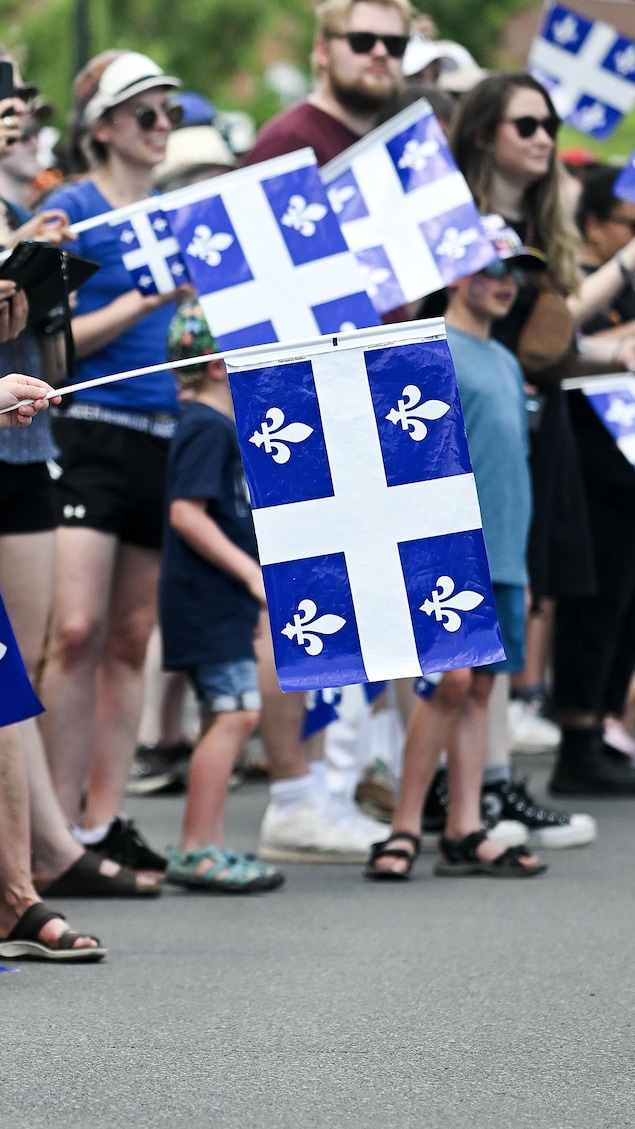 Sur un trottoir, des gens brandisses des drapeaux du Québec.