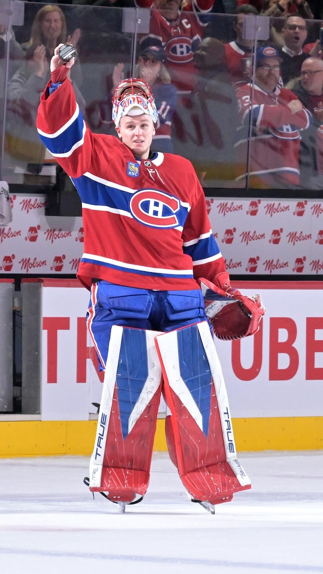 Un gardien de but portant les couleurs du Canadien de Montréal brandit une rondelle sur une patinoire.