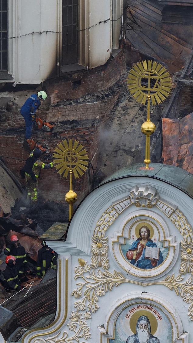 Des pompiers sur le toit d'une cathédrale partiellement incendiée.