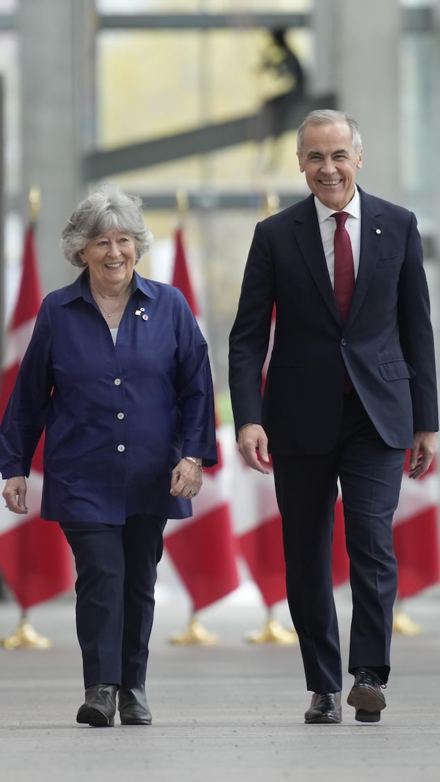Louise Arbour et Mark Carney marchent entre des rangées de drapeaux canadiens.