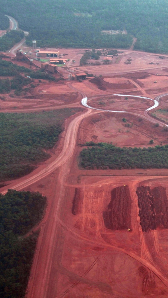 Un complexe minier au sol rouge vif bordé de forêt.