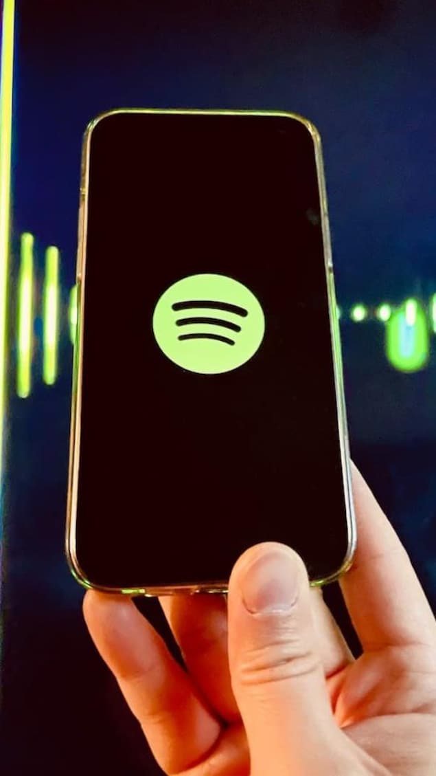 Une main tient un cellulaire ou s'affiche le logo de Spotify.