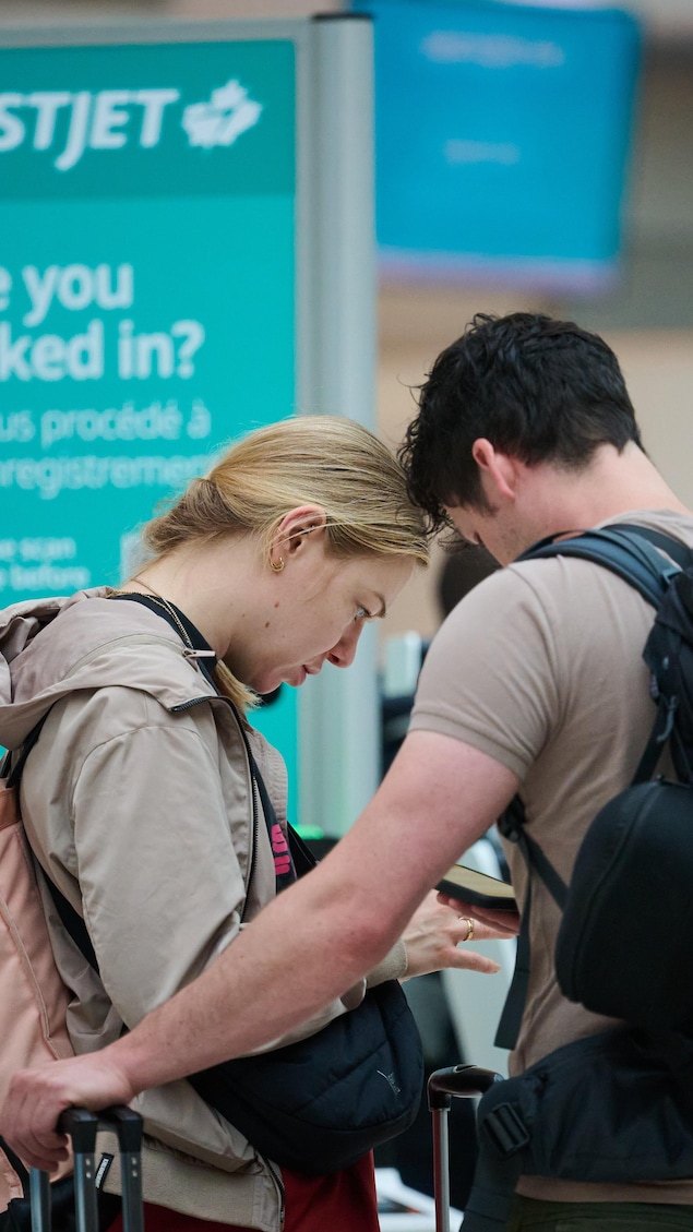 Deux voyageurs regardent leurs téléphones dans un aéroport.