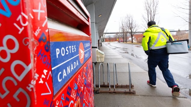 Isang manggagawa ng Canada Post naglalakad habang makikita ang kanilang mailbox.