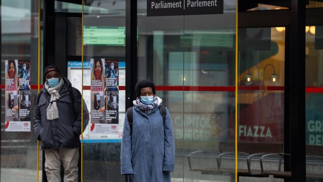 Deux personnes portant le masque attendent à l'arrêt d'autobus.