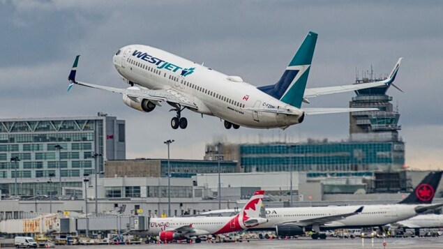 Un avion WestJet décolle dun aéroport. On peut voir des avions d'Air Canada en arrière-plan. 