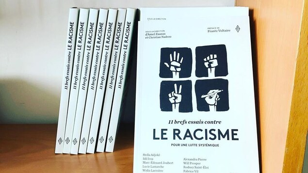 Une pile de livres dans une bibliothèque. L'un d'eux montre une illustration avec quatre mains : une faisant un signe de paix, une ouverte, une fermée en poing et une tenant un crayon.