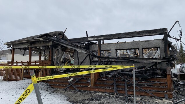 Un ruban jaune de sécurité devant une bâtisse détruite par les flammes. 