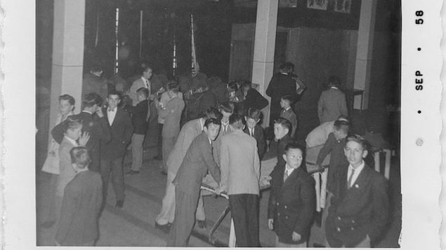 Plusieurs petits groupes de jeunes garçons, qui s'amusent ou discutent dans une salle. À l'avant-plan à droite, un élève portant des lunettes en regarde un autre. qui lui regarde la caméra Plusieurs petits groupes de jeunes garçons, qui s'amusent ou discutent dans une salle. À l'avant-plan à droite, un élève portant des lunettes en regarde un autre. qui lui regarde la caméra