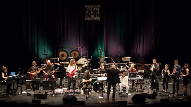 Des musiciennes et musiciens sur une scène jouent sous la direction d'un chef d'orchestre.