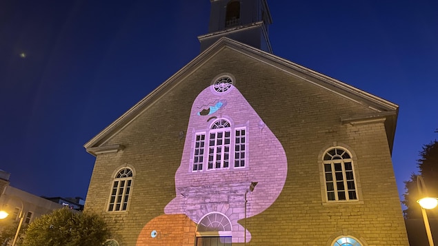 Un gros personnage rigolo avec un seul œil est projeté sur la façade d'une église, la nuit.