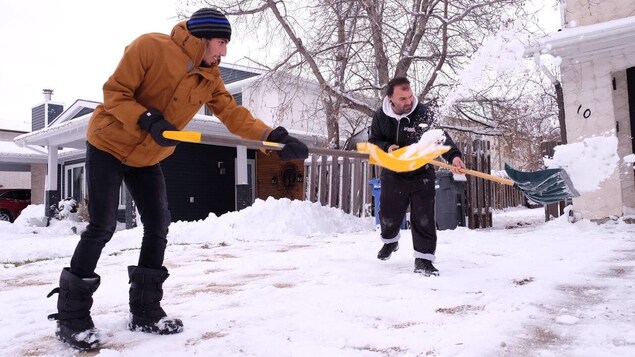 شخصان يزيلان الثلوج من أمام منزل.
