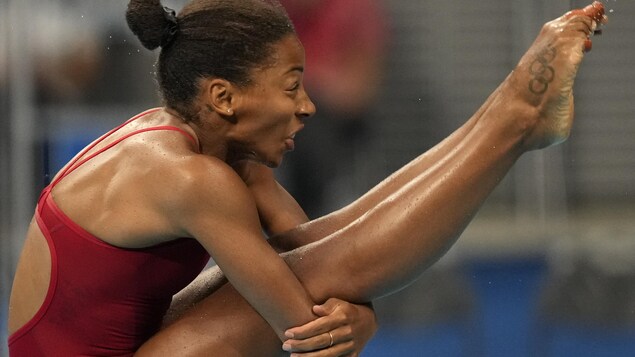 En train de plonger, Jennifer Abel a les jambes droites et est recourbée sur ses jambes. Elle tient l'arrière de ses genoux avec ses deux bras.