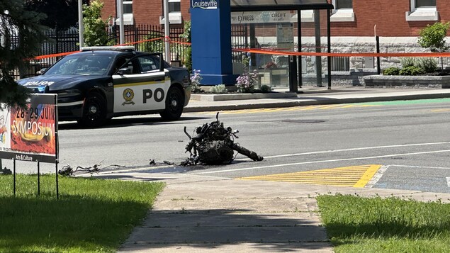 Un véhicule de la Sûreté du Québec est immobilisé sur une rue, près d'un moteur de voiture.