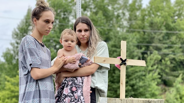 Deux jeunes femmes avec un bébé observent une croix fabriquée à la mémoire des victimes. 