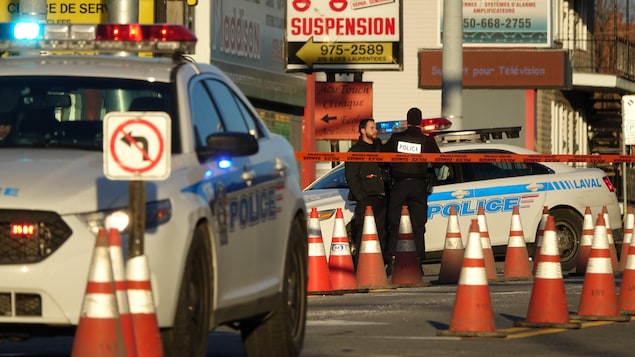 La scène est entourée d'un cordon de sécurité et des policiers discutent entre eux près d'une voiture de patrouille. La scène est entourée d'un cordon de sécurité et des policiers discutent entre eux près d'une voiture de patrouille.