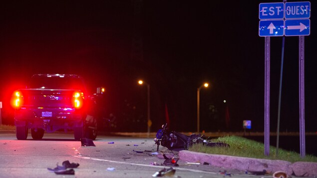 Une camionnette est à l'arrêt. Un scooter est renversé sur la route le soir. Des débris sont sur la chaussée. 