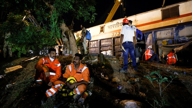 Des secouristes sont assis alors que de la machinerie lourde opère sur le site d'une collision ferroviaire après l'accident dans le district de Balasore, dans l'État oriental d'Odisha, en Inde, le 3 juin 2023.