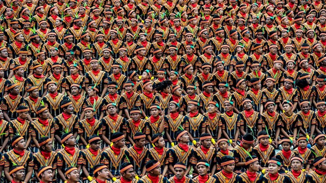 10 000 Indonésiens en habit traditionnel coloré dans les teintes de rouge et d'orange. Chacun est coiffé d'un bandeau portant une plume verte.