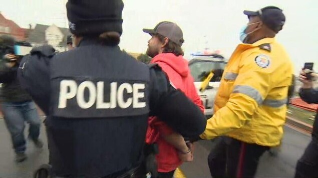 Un homme menotté et encadré par deux policiers en uniforme, à l'extérieur.