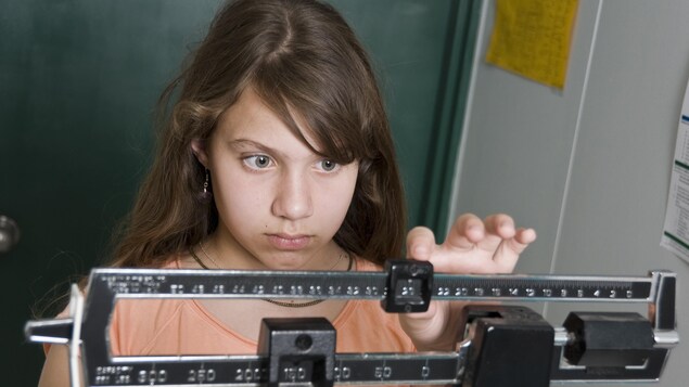 Une jeune fille se pèse sur la balance, elle a l'air inquiète à propos de son poids.