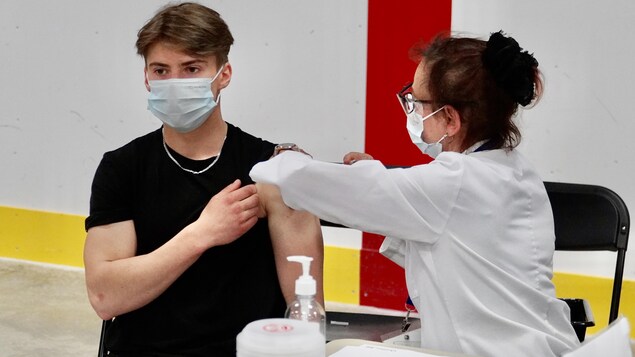 Une infirmière injecte une dose de vaccin dans l'épaule d'une jeune homme.              