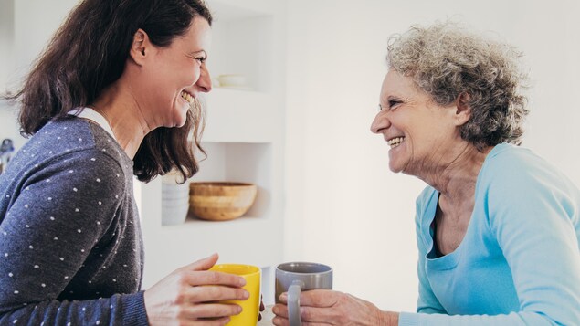 Une femme adulte et sa mère âgée devant des tasses de café.