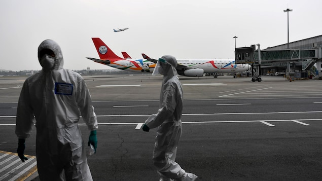 Deux hommes en combinaison et masqués sur le tarmac d'un aéroport.