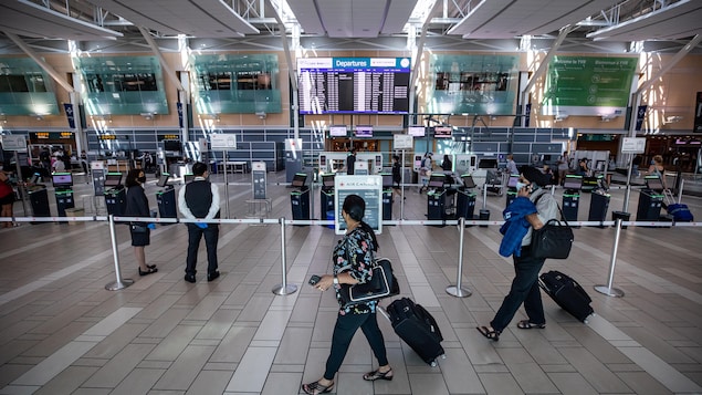 Des voyageurs, valises à la main, passent devant la zone d'enregistrement d'Air Canada dans un aéroport.